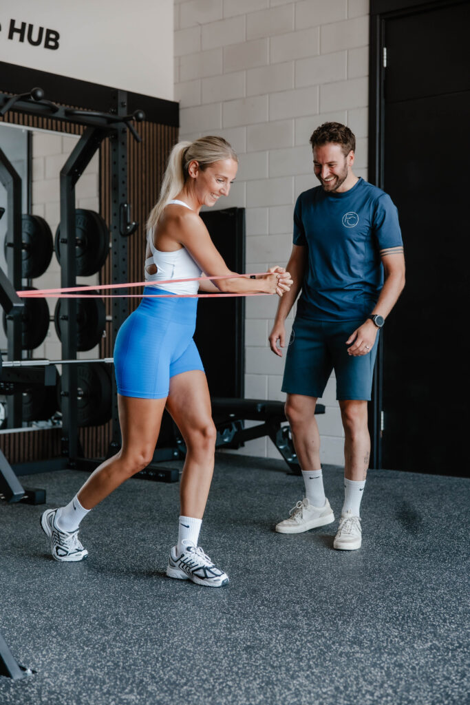 Coach begeleidt een sporter bij een oefening met een weerstandsband in de Performance HUB